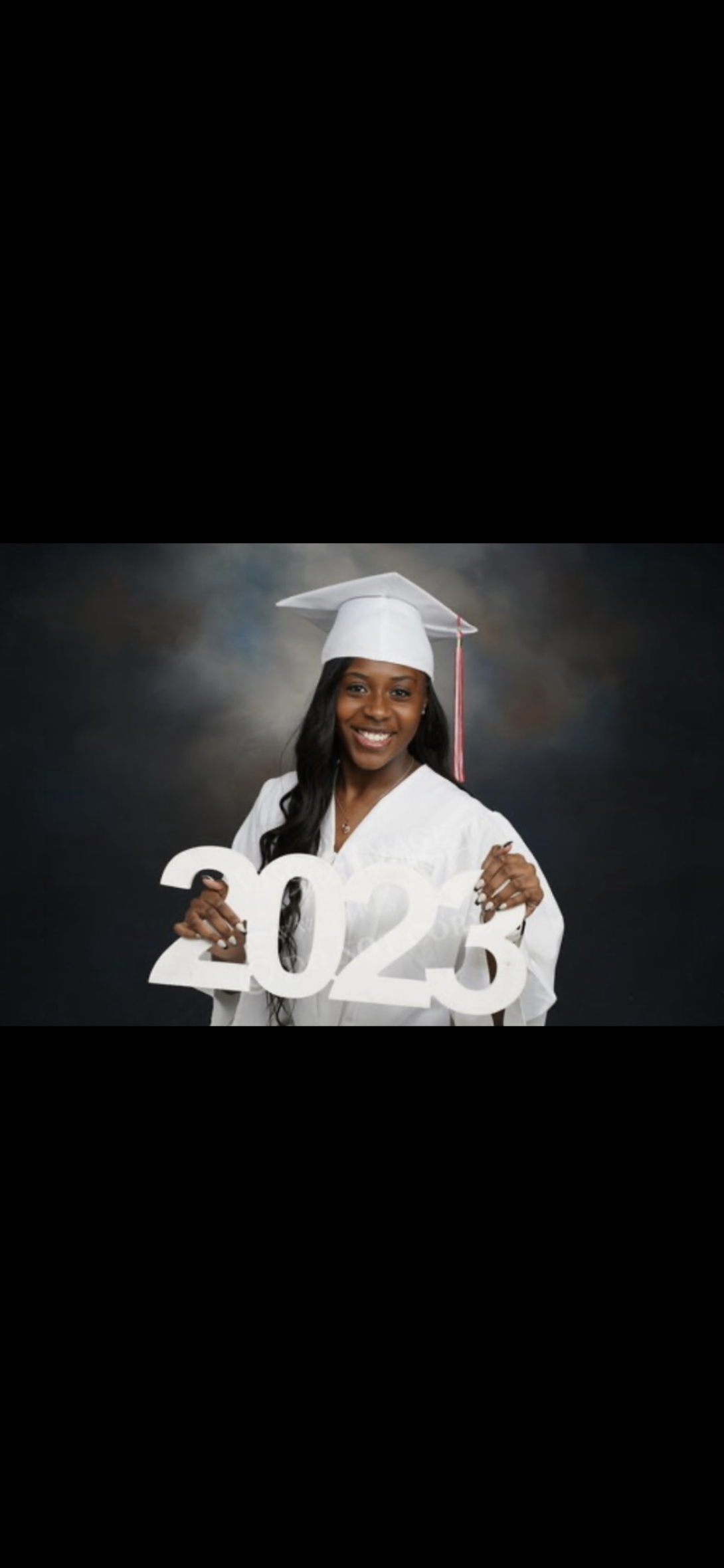 Photo of student in cap and gown holding up 2023 sign